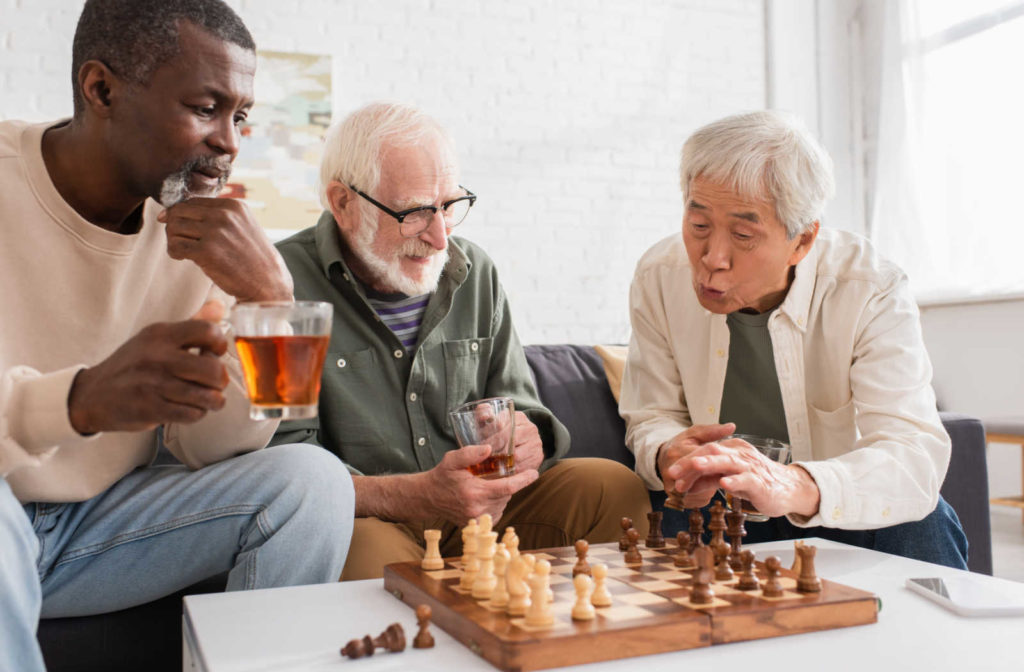 Three elderly men sitting next to each other at a table playing a game of chess in a senior living facility.