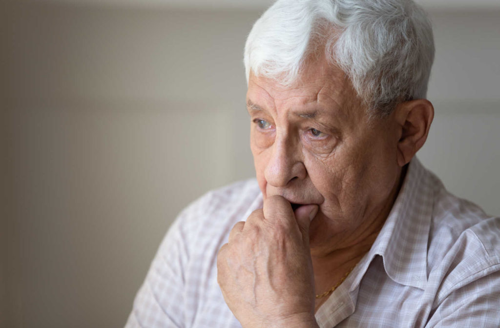 An elderly man lost in deep thoughts with his hand on his chin.