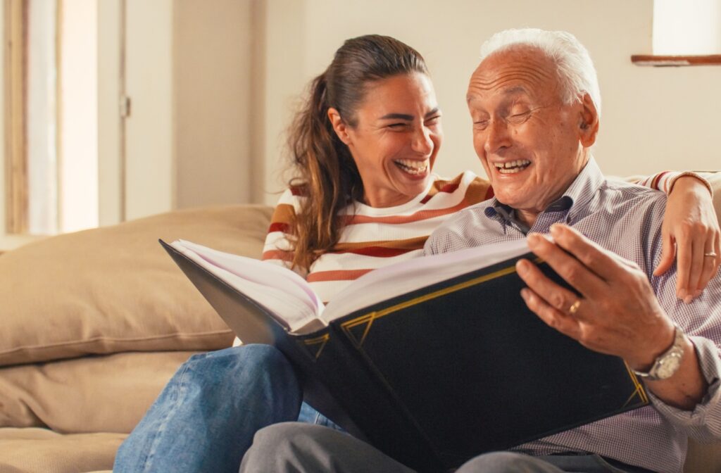 A senior man and his daughter smiling while looking at a photo album together.