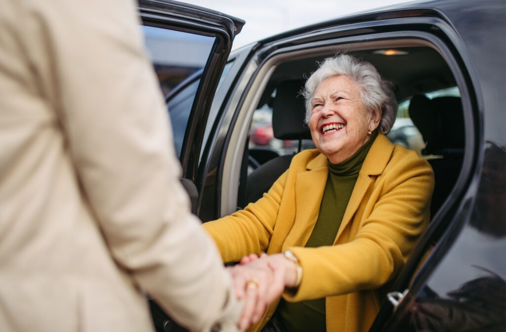 A senior gets out of a vehicle with the help of a community team member.