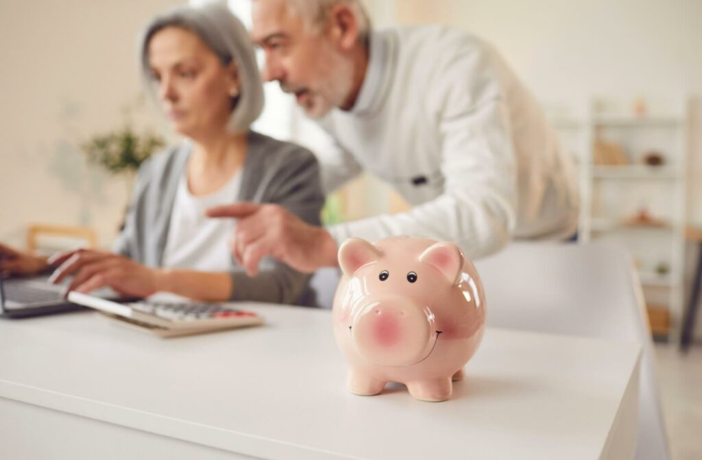 Two seniors using a laptop to manage their finances with a calculator and piggy bank in the foreground